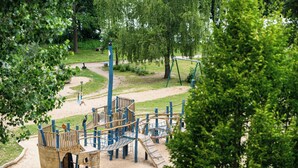 Ein Spielplatz mit Klettergerüsten und einer Rutsche, umgeben von Bäumen und einem Sandbereich.