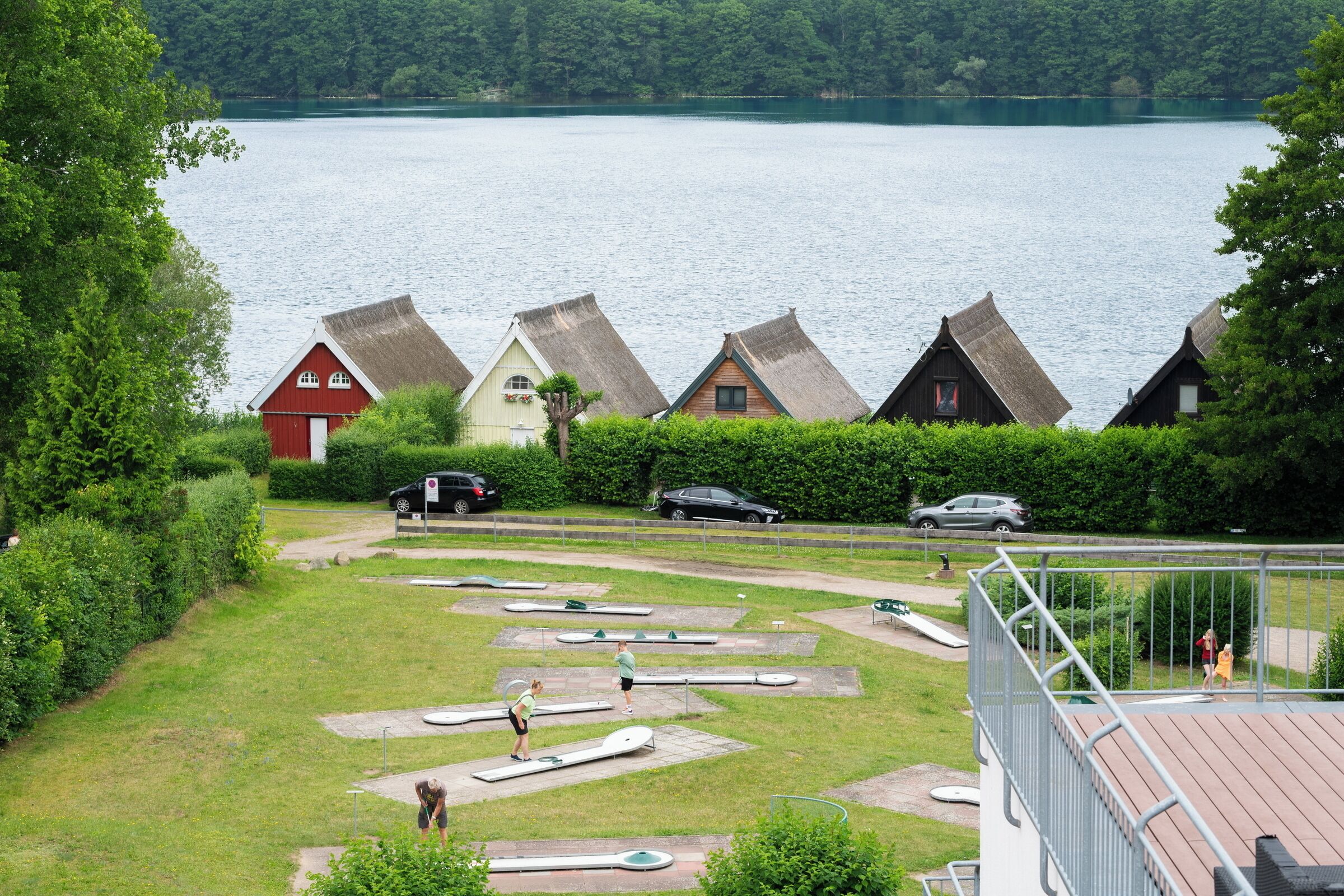 A lakeside view with traditional houses, a swimming area, and a parking lot.