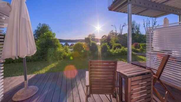 Eine Holzterrasse mit Tisch und Stühlen, mit Blick auf eine malerische Landschaft mit Bäumen und einem Gewässer.