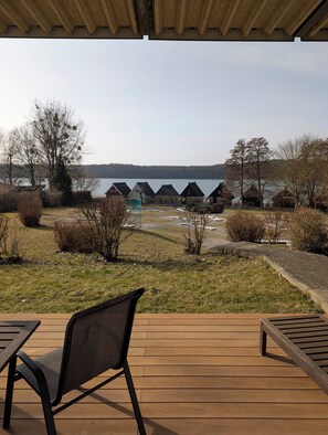 Een houten terras met stoelen, uitzicht op een meer en verschillende cottages met rieten daken.