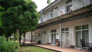Ein modernes Gebäude mit überdachter Außenbereitschaft, inklusive eines Balkons mit Metallgeländern und einer Sitzecke mit Stühlen und Tisch.
