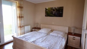 A bedroom with a double bed, two bedside tables, a radiator, and a window with curtains.