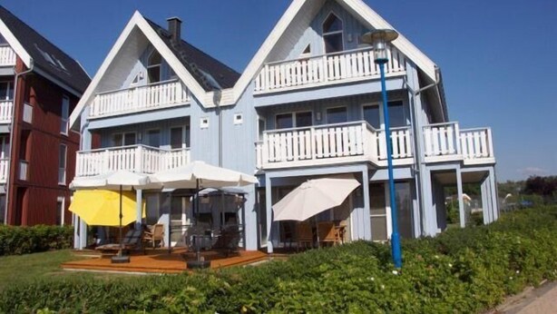 A two-story building with a balcony on each floor, a covered outdoor seating area, and a clear sky.