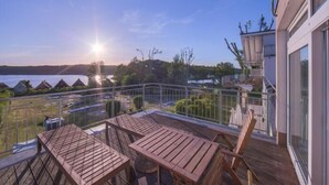 Eine Holzdielen-Terrasse mit Tischen und Stühlen, die auf ein Gewässer und eine bewaldete Landschaft blickt.