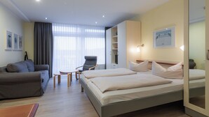Ein modernes Hotelzimmer mit Bett, einer Couch, einem Sessel, einem kleinen Tisch und einem Kleiderschrank.