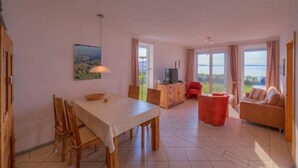 A spacious living area with a dining table, chairs, a sofa, and a TV on a wooden cabinet.