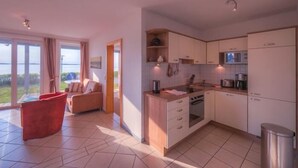 A modern kitchen with white cabinets, a microwave, and a sink. There is a red chair and a sofa in the living area.