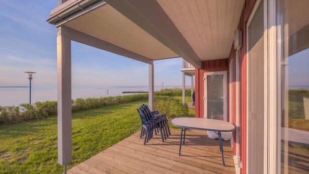 A covered outdoor area with a wooden deck, a table with chairs, and a view of the sea.