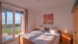 A bedroom with a large bed, two bedside tables, a nightstand, and a painting on the wall.
