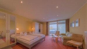 Ein Hotelzimmer mit einem Bett, einem Schlafsofa, einem Sessel, einem kleinen Tisch und einem Fenster mit Vorhängen.
