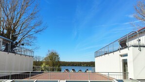 Eine Dachterrasse mit Glasgeländern, Blick auf einen See und eine bewaldete Landschaft.