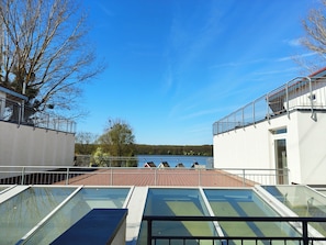 A rooftop terrace with glass balustrades, a view of a lake, and a forested landscape. - Strandläufer Classic 214 - Apartment mit Sitzecke für 2 Personen im Aparthotel (Mirow Ortsteil Granzow)