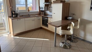 Una cocina moderna con comedor, que presenta una mesa de madera, sillas blancas y un horno empotrado.