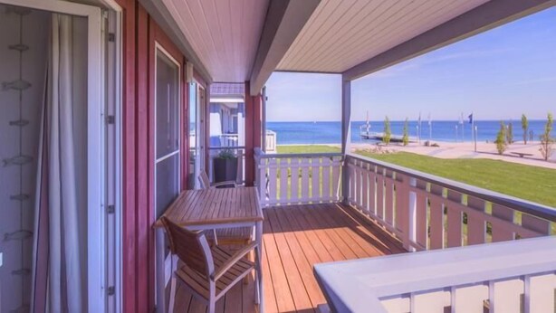 Una terraza de madera con una mesa y sillas, con vista a una playa y una vista despejada del océano y algunas banderas.