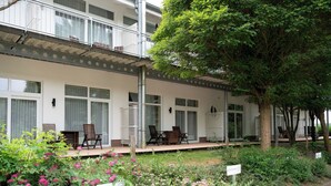 Un hotel con un área de estar exterior cubierta, un jardín con flores rosadas y un árbol.