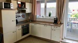 A compact kitchen with a microwave, stove, sink, and cabinets. There is a window with curtains and a view of the outside.