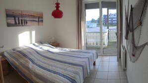 A bedroom with a bed, a nightstand, a red pendant light, a painting on the wall, and a view of the outside through a sliding glass door.