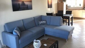 A modern living room with a blue sofa, a wooden coffee table, and a painting of a sunset over a pier.