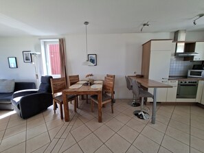 A modern kitchen with a dining table, chairs, and a sofa in a living area. - Mitteldeck 424 - Gemütliches Ferienapartment mit Blick auf die Müritz (Rechlin-Nord)