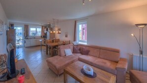 Una sala de estar moderna con un sofá modular, una mesa de centro de madera y un comedor con mesa y sillas.