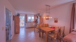 Un comedor amplio con una mesa y sillas de madera, una cocina al fondo, y vistas al exterior a través de una ventana.