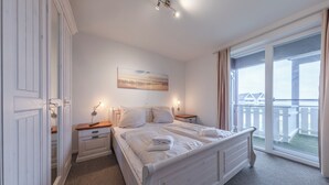A bedroom with a large bed, a nightstand, a dresser, a painting on the wall, and a balcony with a view. - Mitteldeck 464 - Gemütliches Ferienapartment mit Blick auf die Müritz (Rechlin-Nord)