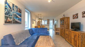 A living room with a blue sofa, wooden coffee table, and a TV on a wooden cabinet. - Mitteldeck 464 - Gemütliches Ferienapartment mit Blick auf die Müritz (Rechlin-Nord)