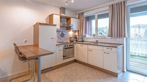 A modern kitchen with a built-in oven, a coffee maker, and a window with curtains. - Mitteldeck 464 - Gemütliches Ferienapartment mit Blick auf die Müritz (Rechlin-Nord)