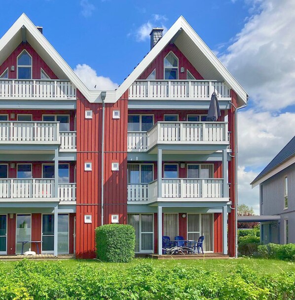 Ein mehrstöckiges Gebäude in Rot und Weiß mit Balkonen, einem kleinen Garten und Außenplätzen.