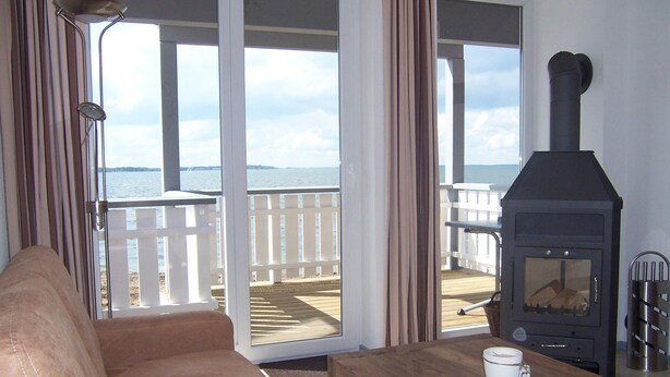 A living room with a sofa, a table with a coffee cup, a wood-burning stove, and a view of the sea through a glass door.