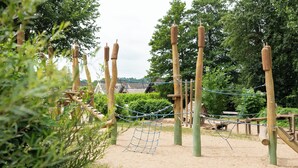 A playground with a rope bridge, wooden posts, and a netted area.