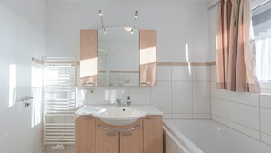 A modern bathroom with a white sink, wooden cabinets, a large mirror, and a bathtub.
