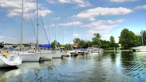 A marina with multiple sailboats docked in calm waters, surrounded by trees and a clear sky. - Mitteldeck 504 - Cozy vacation apartment with a view of the Müritz (Rechlin-Nord)