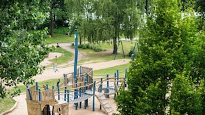 Un parque infantil con estructuras para escalar y un tobogán, rodeado de árboles y una zona de arena.