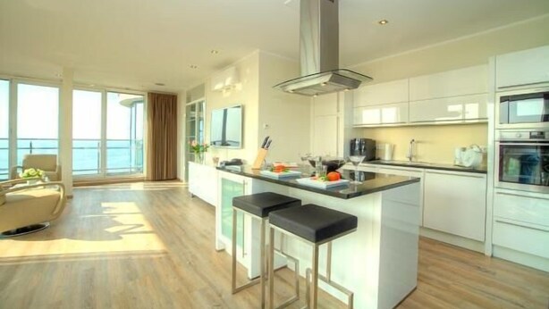 A modern kitchen with a central island, bar stools, and a view of the ocean through large windows.