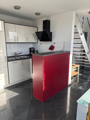 Una cocina moderna con armarios blancos, una isla roja y una escalera.