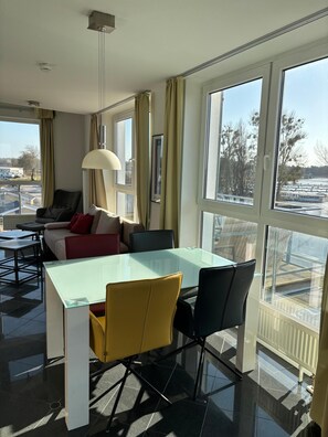 Una habitación moderna con una mesa de vidrio, sillas, un sofá y un amplio ventanal con vistas al exterior.