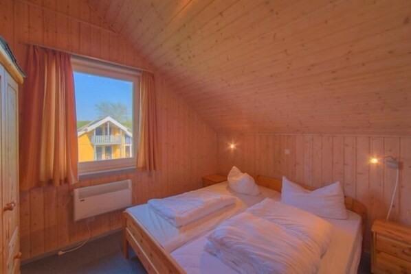 Acogedora habitación de cabaña de madera con dos camas, una ventana y un radiador.