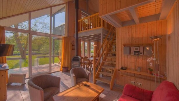 Amplia sala de estar con detalles de madera, ventanas grandes y una escalera que conduce a un nivel superior.