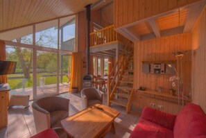 Amplia sala de estar con detalles de madera, ventanas grandes y una escalera que conduce a un nivel superior.