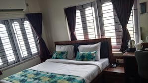 A bedroom with a bed, two pillows, a bedside table with a kettle and a phone, and windows with curtains. - Hotel Kolkata (Barasat)