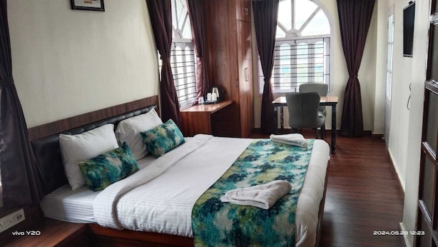 A hotel room with a large bed, a desk, and a chair. - Hotel Kolkata (Barasat)