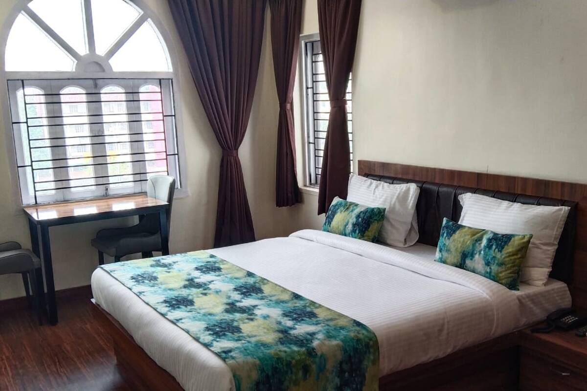 A hotel room with a bed, a desk, and a window with curtains.