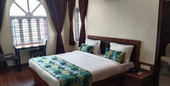 A hotel room with a bed, a desk, and a window with curtains. - Hotel Kolkata (Barasat)