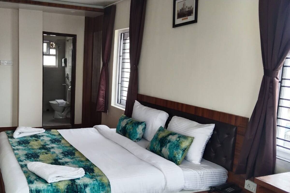 A hotel room with a large bed, a wooden door, a bathroom visible through an open door, and a framed picture on the wall.