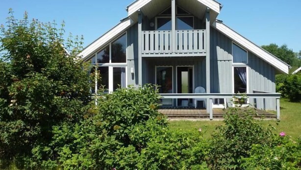 A two-story house with a balcony, surrounded by greenery.
