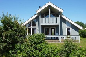 A two-story house with a balcony, surrounded by greenery. - Seeschwalbe Classic 8 - Großzügiges Ferienhaus mit Eigener Sauna und Whirlpool (Rechlin-Nord)