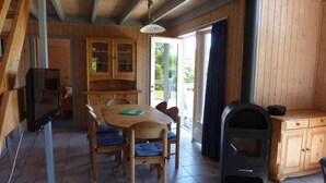 A wooden interior with a dining table, chairs, a built-in stove, and a television.
