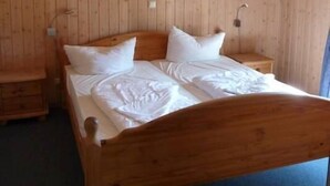 A wooden-paneled room with a bed, a nightstand, and a wall-mounted lamp.