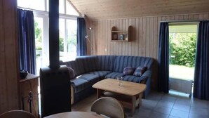 A cozy cabin with a wooden interior, a sofa, a table, and a built-in wood stove.